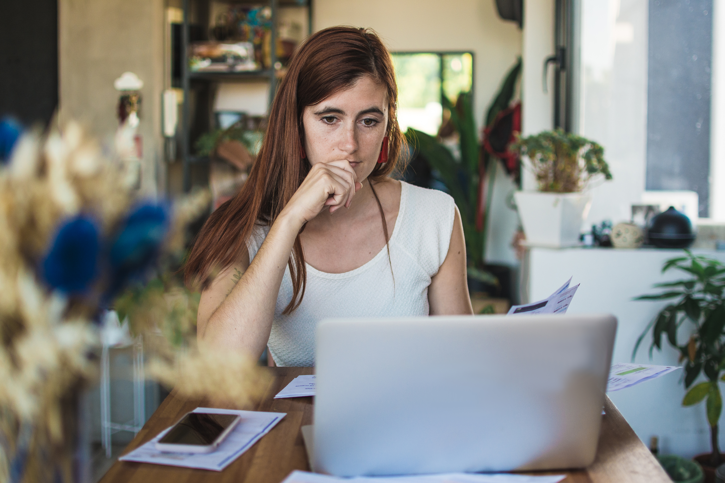 Expense management frustrations. Young woman is sitting at a table with bills, laptop and her phone, working on numbers.