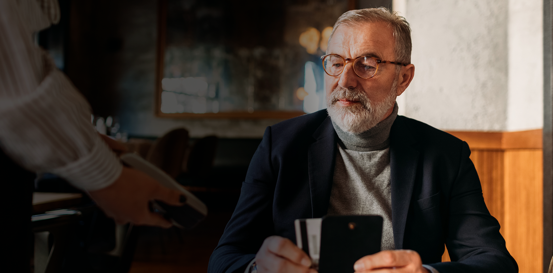 Un homme assis à une table de restaurant paie sa note avec sa carte de crédit