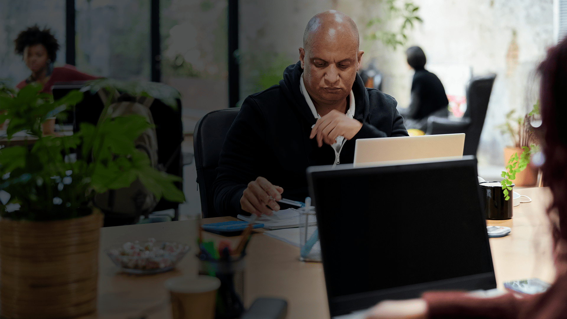 Un homme assis à son bureau devant son laptop tiens un bic entre ses mains
