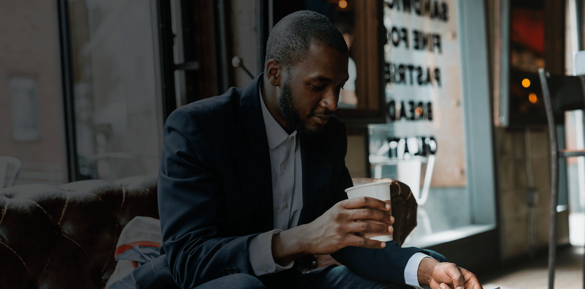 un homme en costume assis dans un bar entrain de boire un café