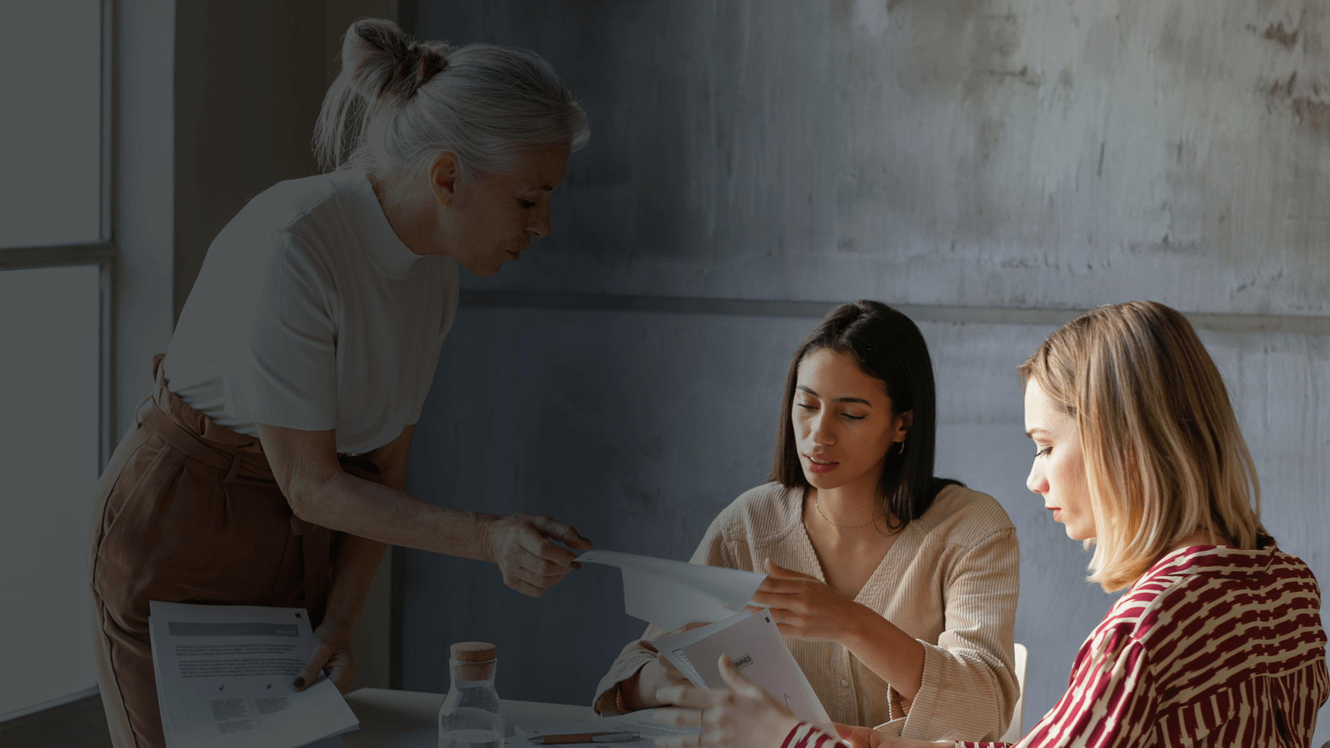 Trois employées à une table, l'une est entrain de montrer des documents à une d'elles