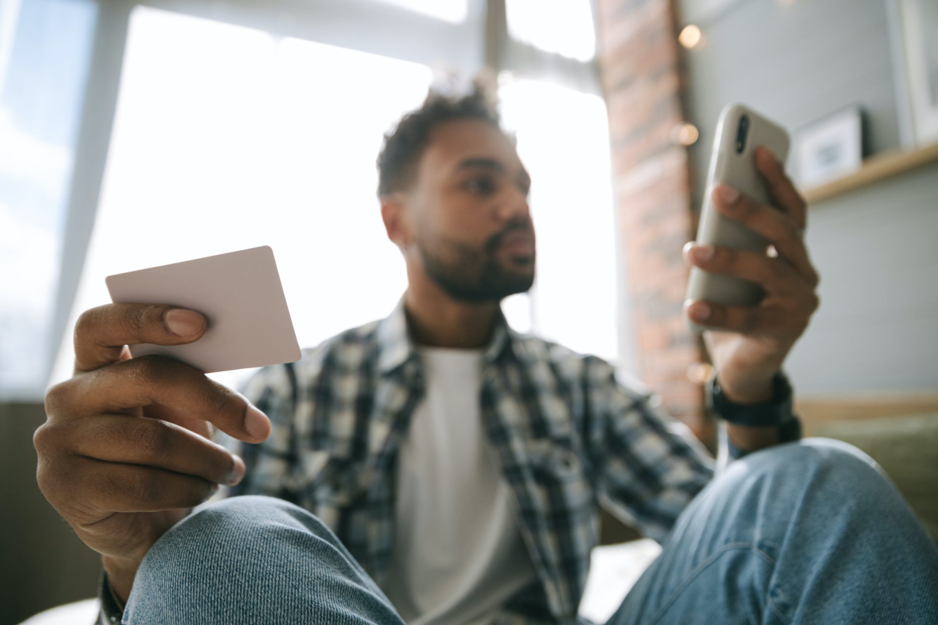 Un homme assis tient son smartphone dans une main et une carte de banque dans l'autre
