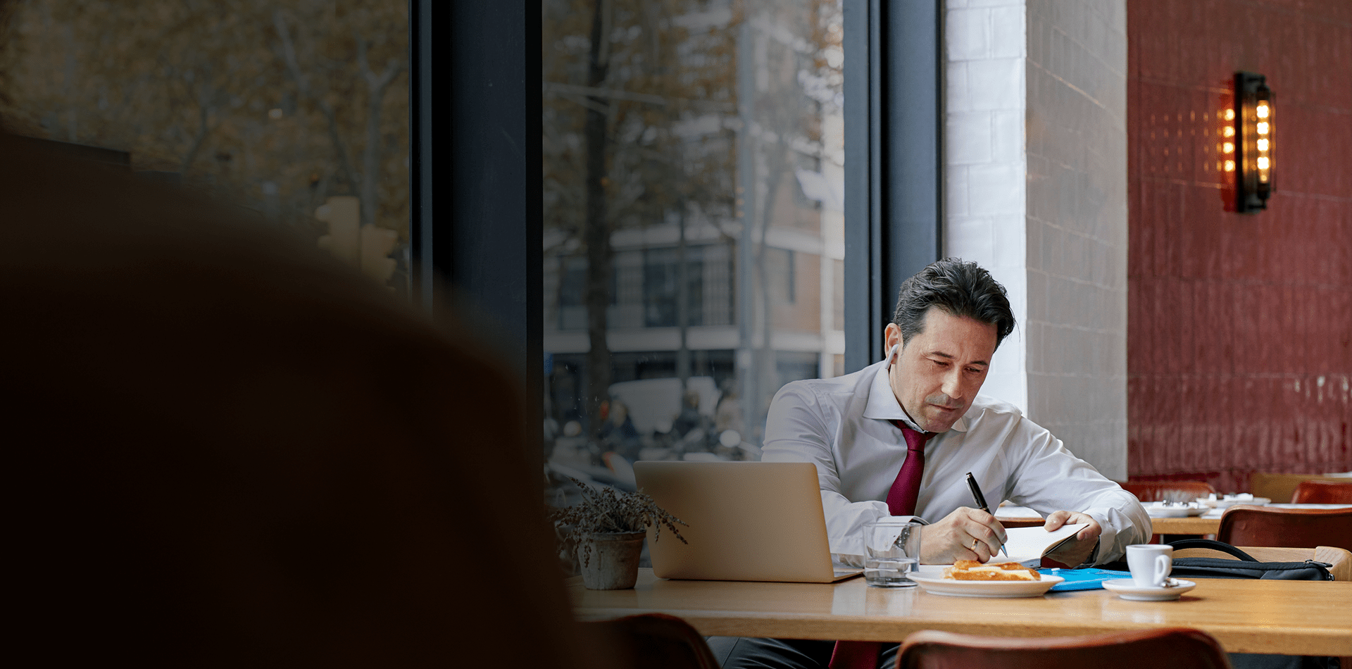 homme d'affaires assis à une table devant un laptop est entrain de prendre des notes