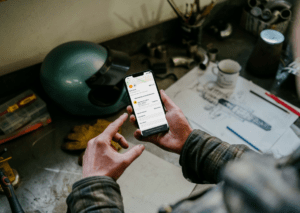 FR Man holding an iPhone 13 Pro mockup over a mechanic’s table (Mockuuups Studio)