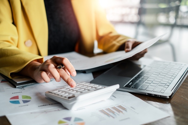 Professional woman reviewing financial charts and data with a calculator and laptop, highlighting business and finance concepts.